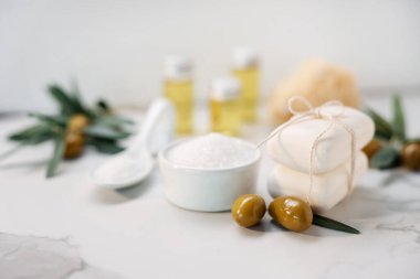 Natural soap bars, olives and sea salt on white marble table, closeup