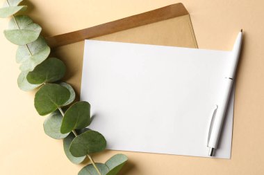 Bej arka planda boş kart, zarf, kalem ve okaliptüs dalı, düz uzanma