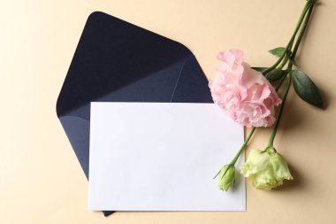 Boş kart, zarf ve çiçekler bej arka planda, düz konum