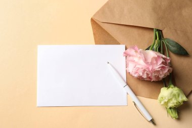 Boş kart, zarf, bej arka planda kalem ve çiçekler, düz konum