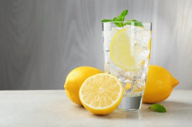 Limon meyveli ferahlatıcı su, açık gri masada buz ve nane şekeri, yakın plan. Metin için boşluk