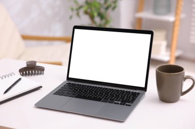 Boş ekranlı modern dizüstü bilgisayar, bir fincan kahve ve beyaz masa üzerinde not defteri. Tasarım için model