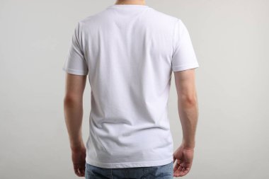 Açık gri arka plan, arka manzara yakınlarında şık beyaz tişörtler giyen genç bir adam. Tasarım için model