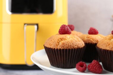 Kürsüde ahududulu enfes fırınlanmış kekler ve gri arka planda hava fritözü, seçici odak