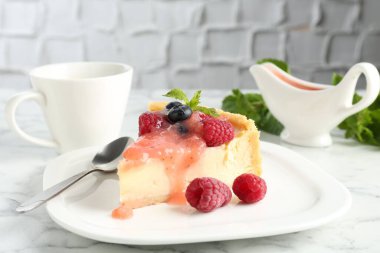 Böğürtlenli ve soslu lezzetli bir cheesecake, beyaz mermer masada servis edilir, yakın plan.