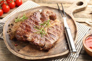 Biberiye, baharat, ahşap masada çatal ve ketçap oymalı lezzetli ızgara biftek, yakın plan.