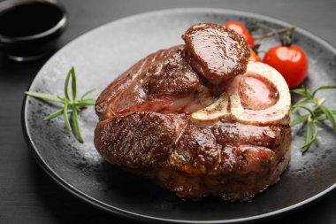Tasty grilled beef steak served with rosemary, sauce and tomatoes on black wooden table, closeup