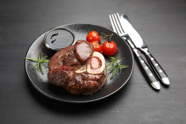 Biberiye, sos, domates ve siyah ahşap masada servis edilen leziz ızgara biftek.