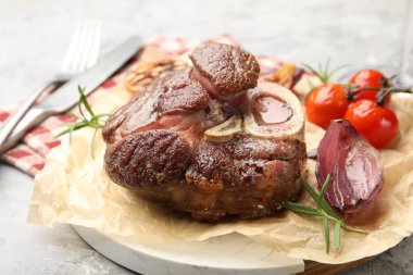 Tasty cut beef steak served with rosemary, garlic and tomatoes on grey textured table, closeup
