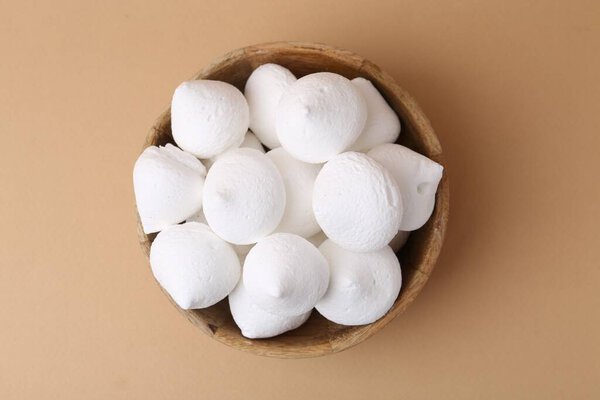 Вкусные безе печенье в миске на бежевом фоне, вид сверху