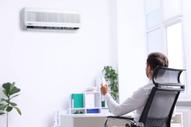 Ofisteki klimayı açmak için uzaktan kumanda kullanan bir adam.
