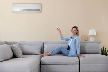 Kadın evdeki koltukta uzaktan kumandayla klimayı açıyor.