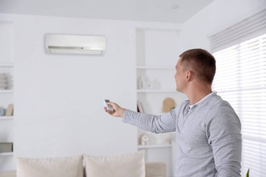 Evdeki adam klimayı uzaktan kumandayla açıyor.