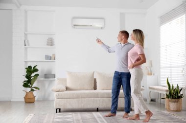 Evde bir çift var. Adam uzaktan kumandayla klimayı açıyor.