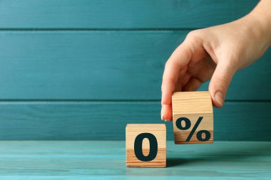 Komisyon yok. Bir kadın, yüzde işareti olan ahşap küpü mavi masanın yanına koyuyor, yakın plan.