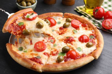 Peynirli, domatesli ve zeytinli lezzetli pizzayı koyu gri masada yakın plan çekiyoruz.