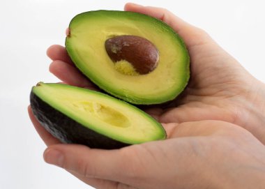 Avocado in female hands. Green ripe fruit. Sliced half with pulp. Healthy diet food. Culinary ingredient. Cooking food. Photo closeup