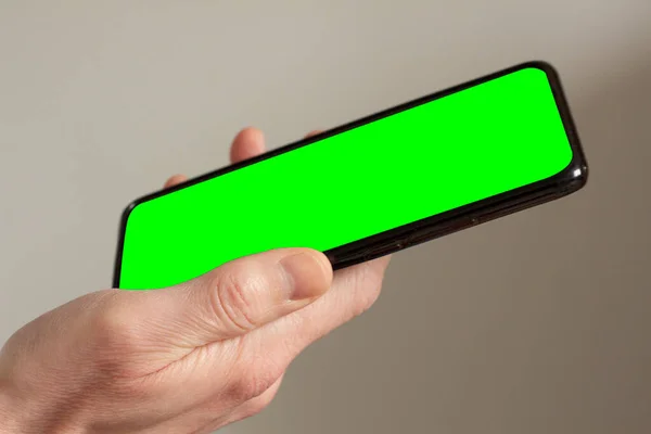 Smartphone in the hands of a man. Looks at the display. Internet search, message exchange. Photo closeup. Green display background