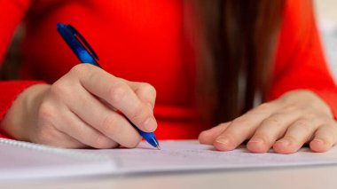 A girl at the table writes with a pen in a notebook. Student studying, taking notes. School and education. Closeup photo