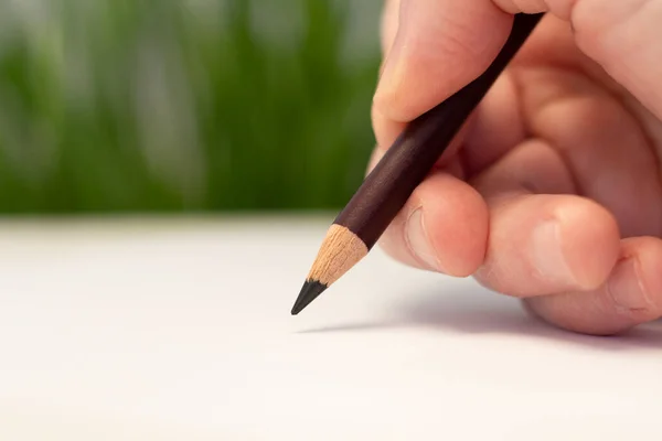 A male hand draws with a pencil on a piece of paper. Artistic tool. Idea, hobby and creativity. Closeup photo