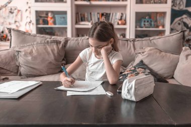 Evdeki oturma odasında ödev yapan bir kız.