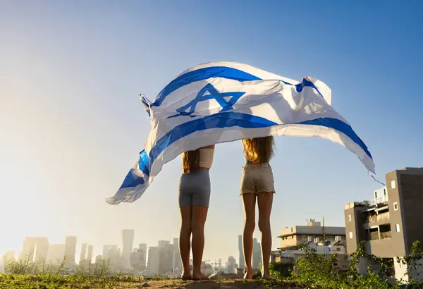 イスラエル国旗を鉄のドームとして振る二人の少女 彼らはジヴァイエイムの地平線を見ている Yom Haatzmaut またはイスラエルのコンセプトとスタンド — ストック写真