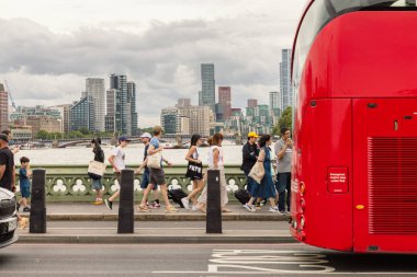 Londra, İngiltere - AUG 03, 2024 - Kırmızı bir otobüs Westminster Köprüsü 'nde yürüyen insanları gösteriyor. Arka planda Thames Nehri ve şehrin ufuk çizgisi görülüyor.