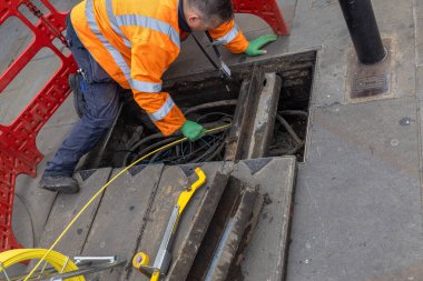 Telefon ya da iletişim alanında çalışan bir teknisyen, bazı sorunları çözmek için sokaktaki bir deliğe yeni kablolar yerleştiriyor.