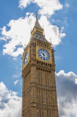 Londra, İngiltere 'deki ikonik saat kulesi Big Ben' in yakın görüntüsü. Saat yüzü karmaşık ayrıntılarıyla görünür ve kule kabarık bulutlu mavi gökyüzüne karşı yükselir.