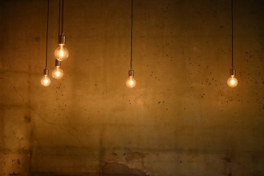 Orange hanging light bulb against old cement wall