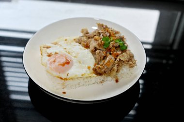 Kutsal fesleğenle kızarmış tavuk ve beyaz tabakta kızarmış yumurta.