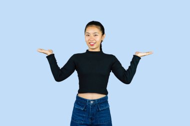 Siyah bluzlu bir kadın, ürün tanıtımı için mavi arka planda ellerini tutuyor.