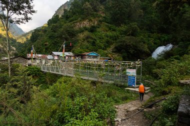 Syafrubesi, Rasuwa, Nepal - October 13 2024 : Syafrubesi to Bamboo Route in Langtang Valley Trek with Shops suspension bridge and waterfalls in front of a tea house lodge  clipart