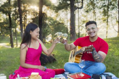 Romantik çift doğada buluşuyor, yemekle piknik yapıyor, gitar çalıyor ve güneşin tadını çıkarıyor.