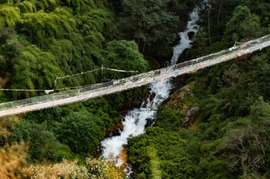 Yukarı Syafru Nepal 'deki yeşil ormanın ortasındaki bir buzul nehri üzerindeki asma köprü.