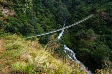 Yukarı Syafru Nepal 'deki yeşil ormanın ortasındaki bir buzul nehri üzerindeki asma köprü.