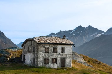 Arka planda görkemli İsviçre Alpleri ile, yemyeşil çayırlar ile çevrili, yüksek irtifada tünemiş eski bir dağlık ev.