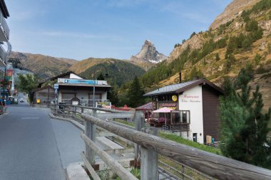 Zermatt, Visp, İsviçre - 19 Ağustos 2025: Zermatt, İsviçre 'de sabahın erken saatlerinde büyüleyici pansiyonlar, dükkanlar ve restoranlar güneş ışığıyla yıkandı ve muhteşem Matterhorn kulesi arka tarafta.