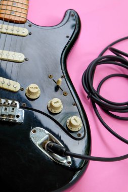 Pembe arkaplanda kablo olan elektro gitar, yakın plan görüntü.