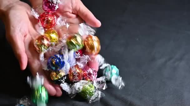2022年8月 奥地利维也纳 令人惊奇的慢镜头林德松露巧克力球包裹着五彩斑斓的箔 他的手放在黑桌上 — 图库视频影像
