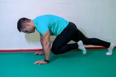 Genç kaslı erkek sporcu, dağ tırmanışı için yer egzersizi yapıyor. Boş duvarlı arkaplan, boşluğu kopyala.