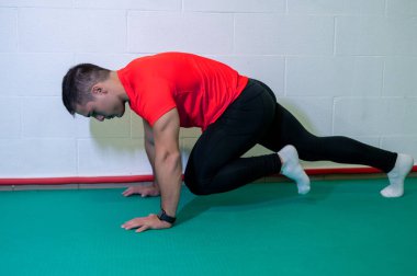 Genç kaslı erkek sporcu, dağ tırmanışı için yer egzersizi yapıyor. Boş duvarlı arkaplan, boşluğu kopyala.