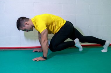 Genç kaslı erkek sporcu, dağ tırmanışı için yer egzersizi yapıyor. Boş duvarlı arkaplan, boşluğu kopyala.