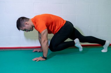 Genç kaslı erkek sporcu, dağ tırmanışı için yer egzersizi yapıyor. Boş duvarlı arkaplan, boşluğu kopyala.