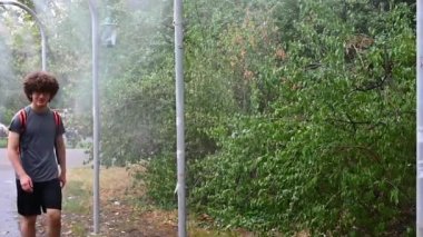 Viyana, Avusturya, Ağustos 2022. Şehir parklarından birinde, su püskürtücülerinin altında yürüyen beyaz bir genç ile güzel bir yavaş çekim görüntüsü. Yaz sıcağına zıtlık kavramı.