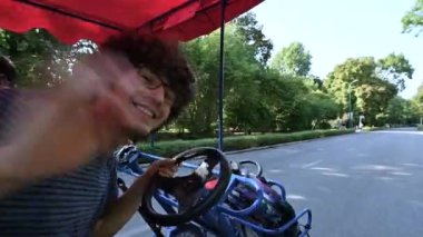 Budapeşte, Macaristan, Ağustos 2022. Pedallı dört tekerlekli bisikletin yolcu koltuğundaki sevimli pov görüntüleri. Direksiyondaki iki adam araca önderlik ediyor ve kameraya bakarken gülümsüyor..