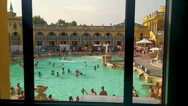 ブダペスト ハンガリー 2022年8月 大規模な露天風呂に向かってSzechenyi風呂の窓の一つから美しいPovの映像 プールは人でいっぱいだ 美しい夏の日 — ストック動画