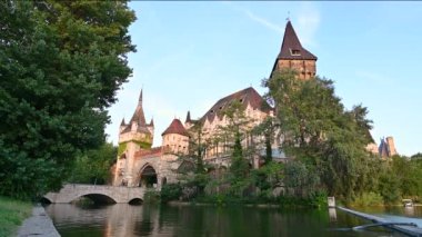 Budapeşte, Macaristan. Ağustos 2022. Geniş açılı mercek ve Vajdahunyad kalesine doğru alçak açılı görüntü. Sıcak öğleden sonra ışığı ön cepheyi aydınlatıyor. İnsanlar köprüden geçiyor..