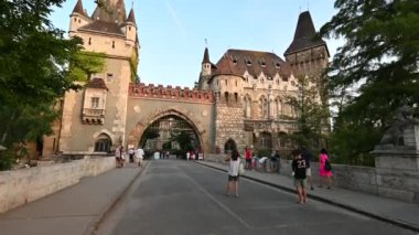 Budapeşte, Macaristan. Ağustos 2022. Baş döndürücü POV görüntüleri Gatehouse Kulesi 'nin girişine doğru yürüyor, sıcak öğleden sonra ışığı ön cepheyi aydınlatıyor. Güzel bir yaz günü, insanlarla karşılaşıyoruz..