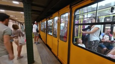 Budapeşte, Macaristan. Ağustos 2022. M1 metro durağındaki görüntüler: en eskisi. Tamamen işlevsel, sarı vagon dolusu insan duruyor ve kapıları açıyor. İnsanlar yukarı aşağı gider..